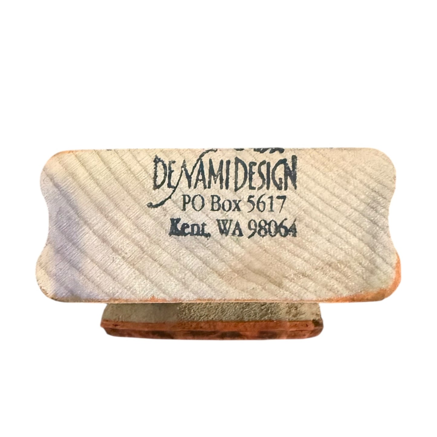 A rectangular wooden stamp block with rounded corners, black printed text reading 'DENAMI DESIGN PO Box 5617 Kent, WA 98064', shown on a plain white background.