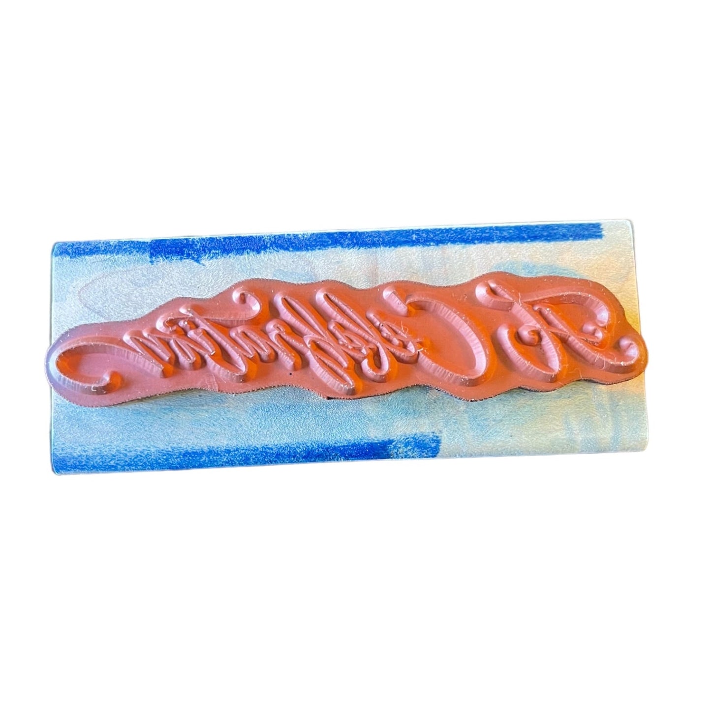A rectangular rubber stamp with embossed script design, set against a white background.