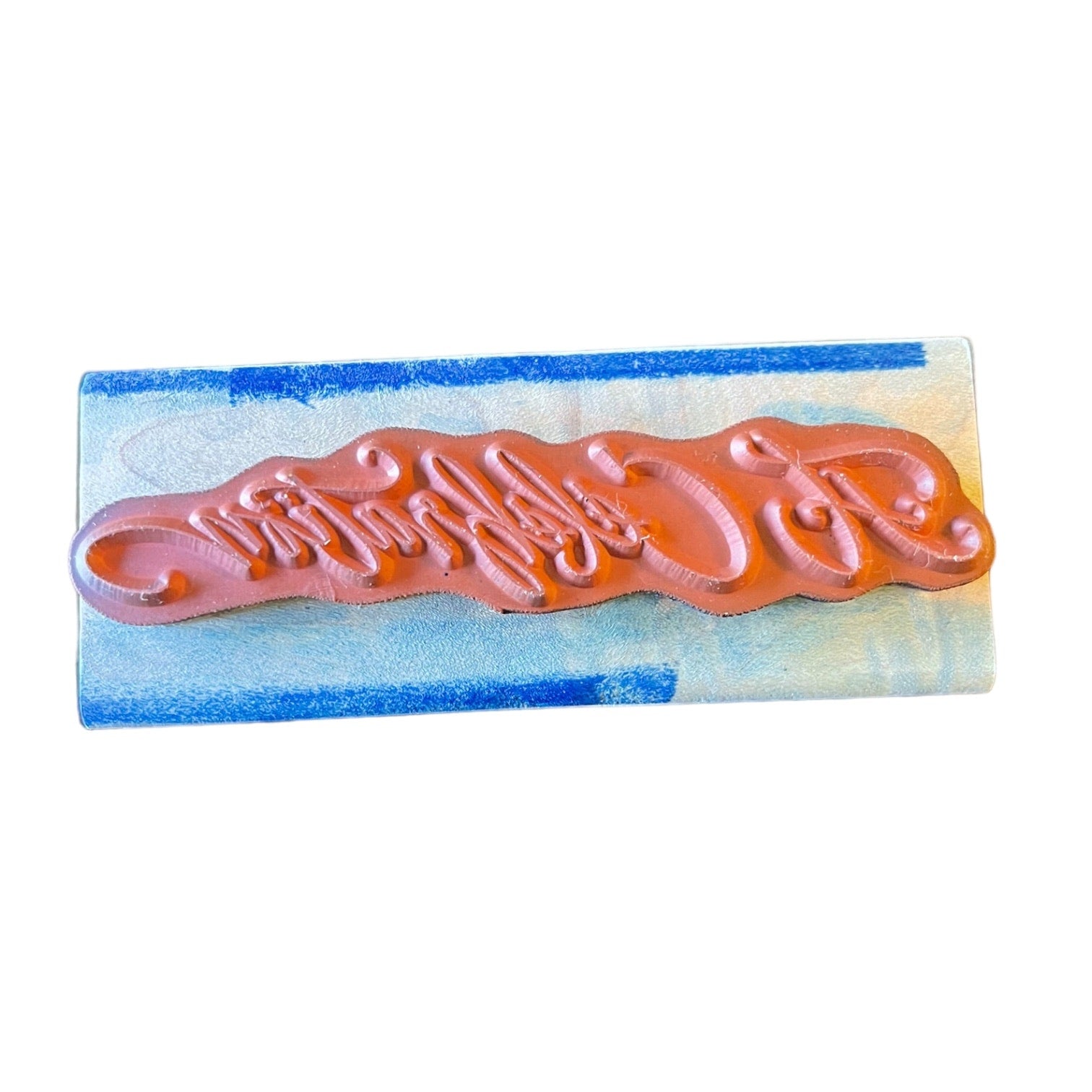 A rectangular rubber stamp with embossed script design, set against a white background.