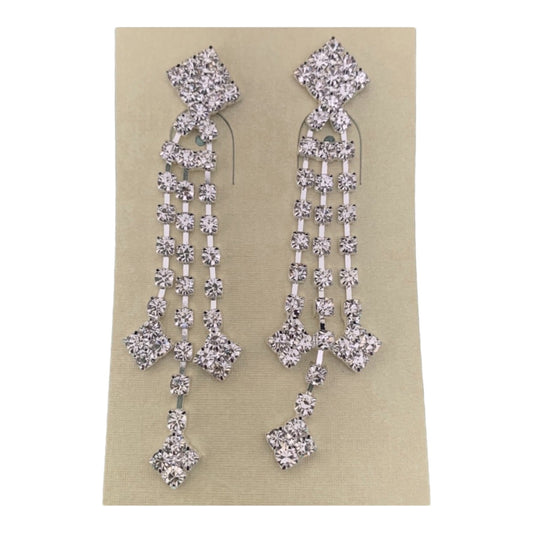 A pair of silver-toned dangle earrings embellished with clear rhinestones in a geometric, multi-tiered design, shown on a beige card against a plain white background.