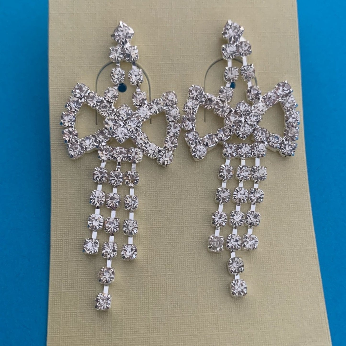 Pair of silver chandelier earrings on a beige card with a blue background