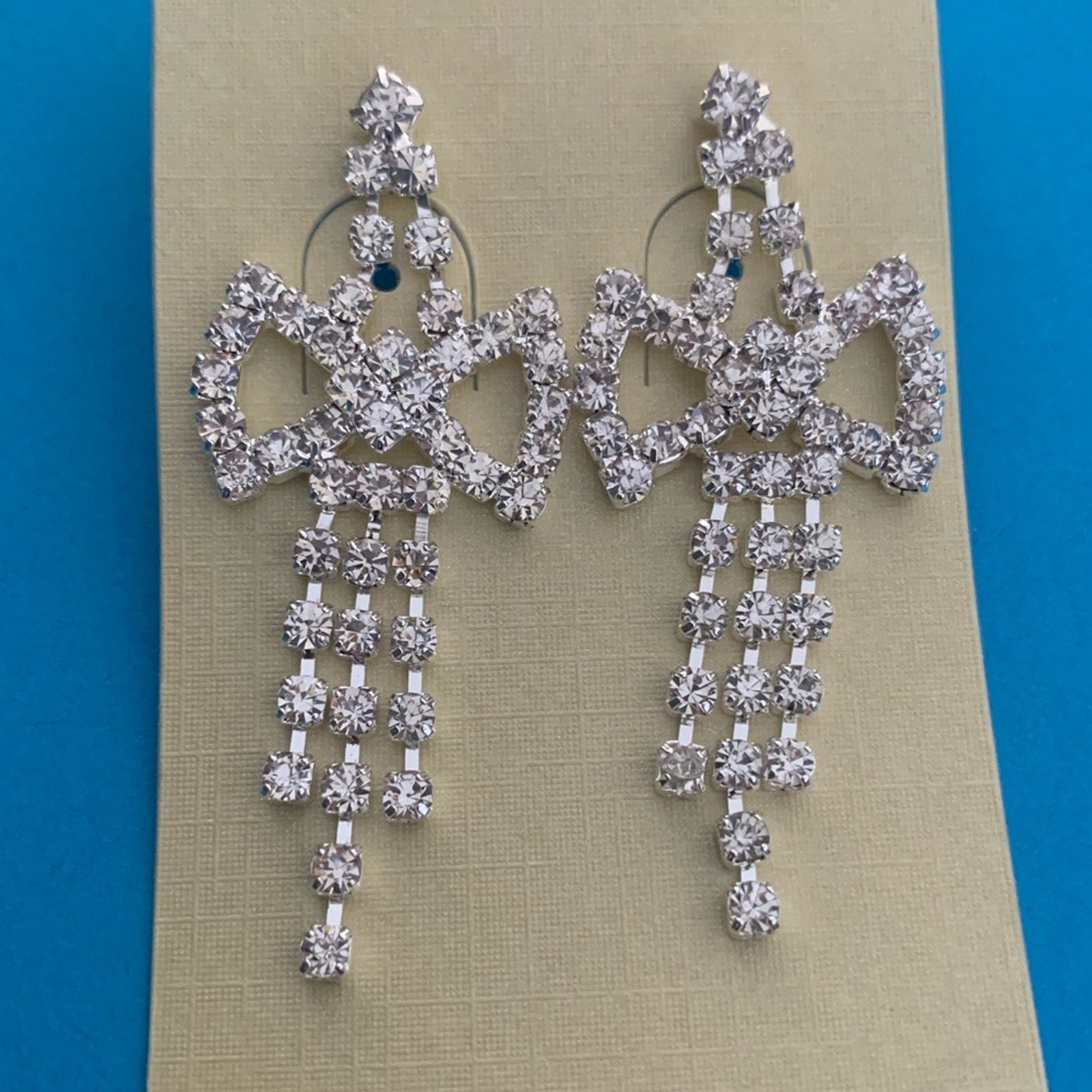 Pair of silver chandelier earrings on a beige card with a blue background
