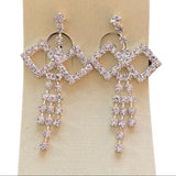 Pair of diamond-shaped earrings with dangling crystals on a beige card.