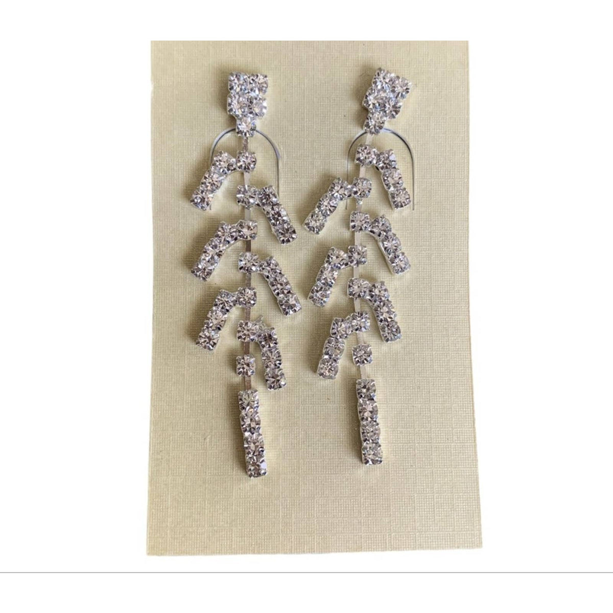 A pair of silver-toned statement earrings with multiple dangling geometric segments with faux diamonds, displayed on a beige fabric card against a white background.