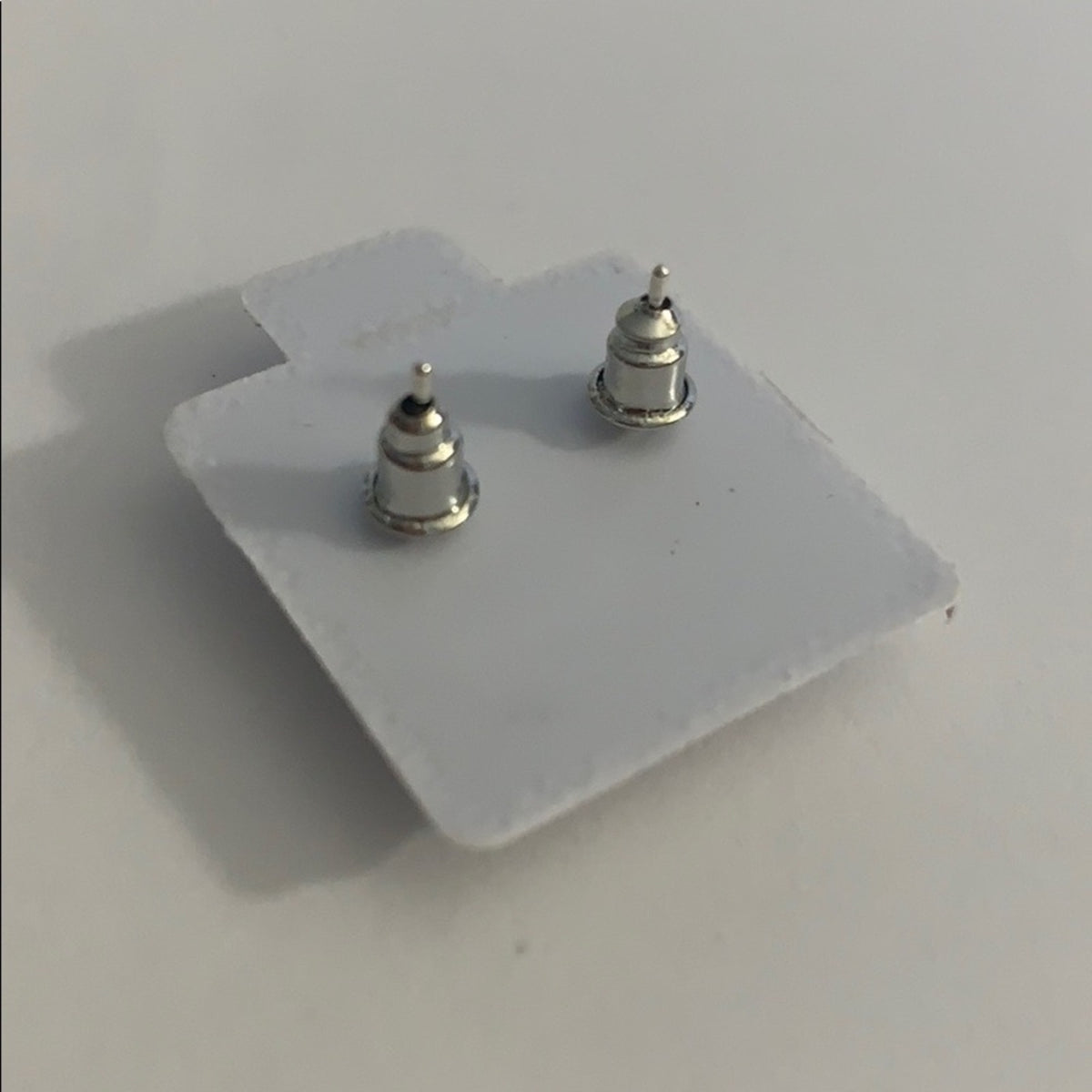 A pair of small silver CZ stud earrings mounted on a white display card, photographed on a plain light gray surface.