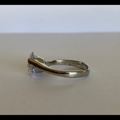 A silver-toned solitaire ring with a clear round-cut gemstone, photographed on a neutral light gray surface.