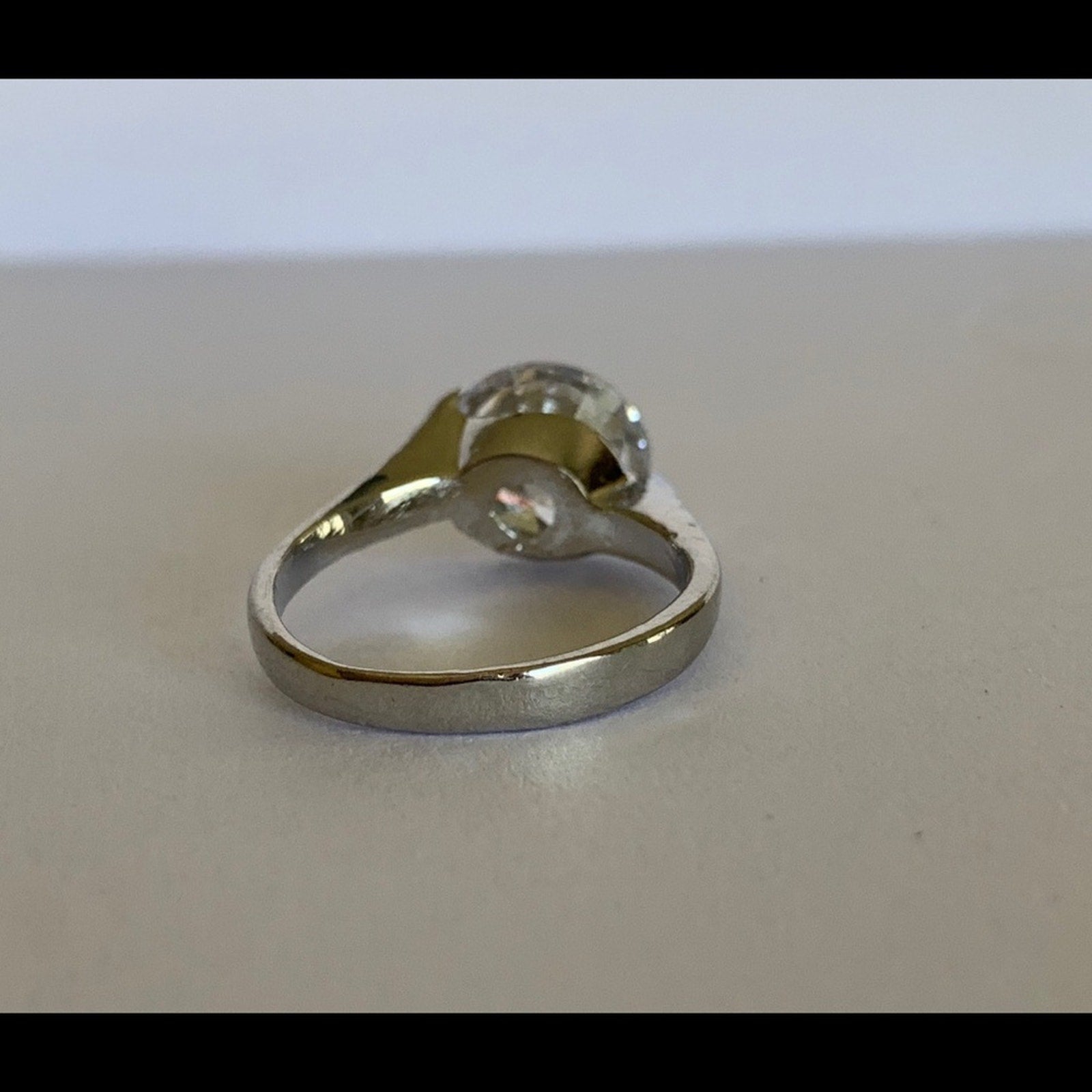 A silver-toned ring with a round clear gemstone photographed on a plain light gray surface.