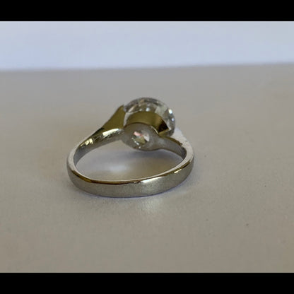 A silver-toned ring with a round clear gemstone photographed on a plain light gray surface.