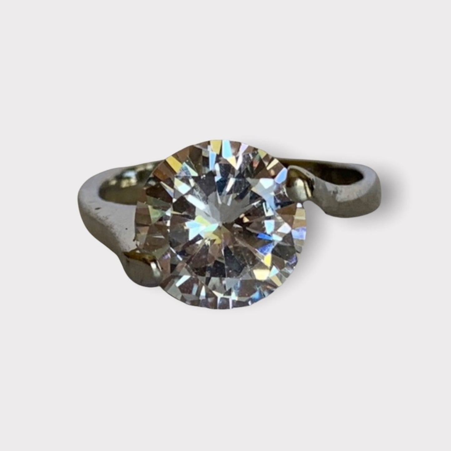 A solitaire ring featuring a large round brilliant-cut clear gemstone set in a silver-colored metal band, shown against a white background.
