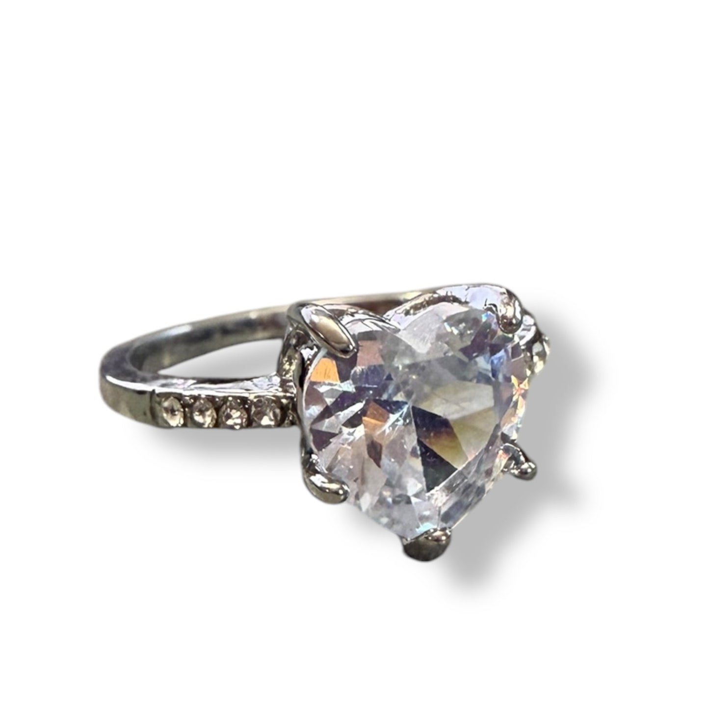 A heart-shaped clear gemstone ring set in a silver-toned metal band with small accent stones on the side, shown on a white background with a soft shadow.