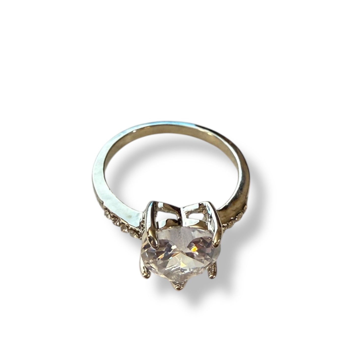 Top view of a heart shaped clear stone ring set in a silver tone ring on a white background. 