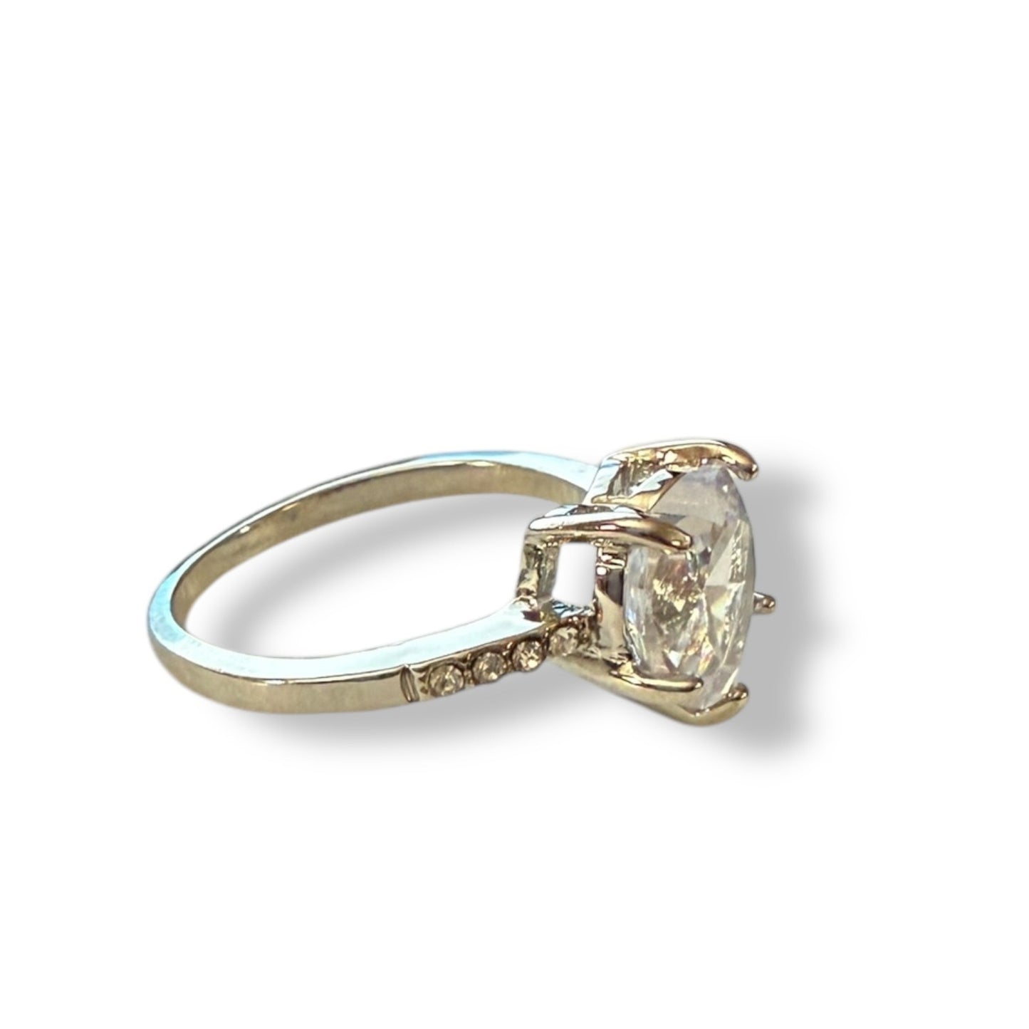 A silver tone ring featuring a large heart clear gemstone in a prong setting, with small accent diamonds along the band, shown on a white background.