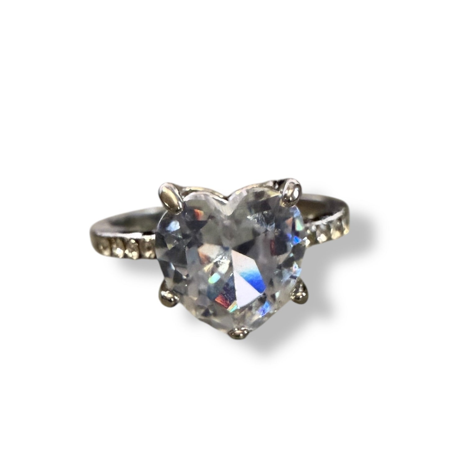 A heart-shaped clear gemstone ring set in a silver-toned metal band with small accent stones on either side, shown on a plain white background.
