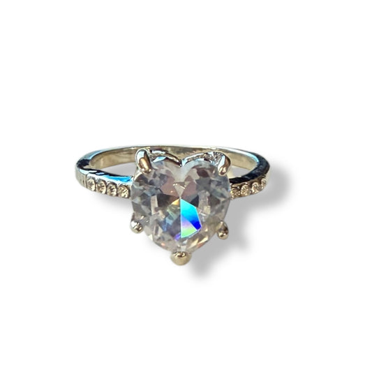 A heart-shaped iridescent gemstone ring set in a silver-colored metal band with small accent stones on either side, shown on a plain white background.