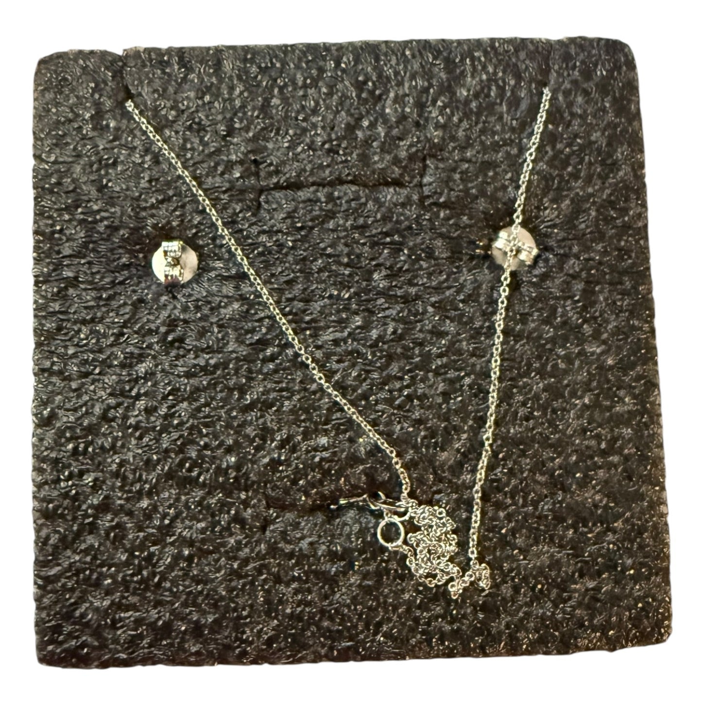 Silver back of necklace and earrings on a textured black surface