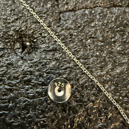 Close-up of a silver chain and earring with a '925' stamp on a textured surface