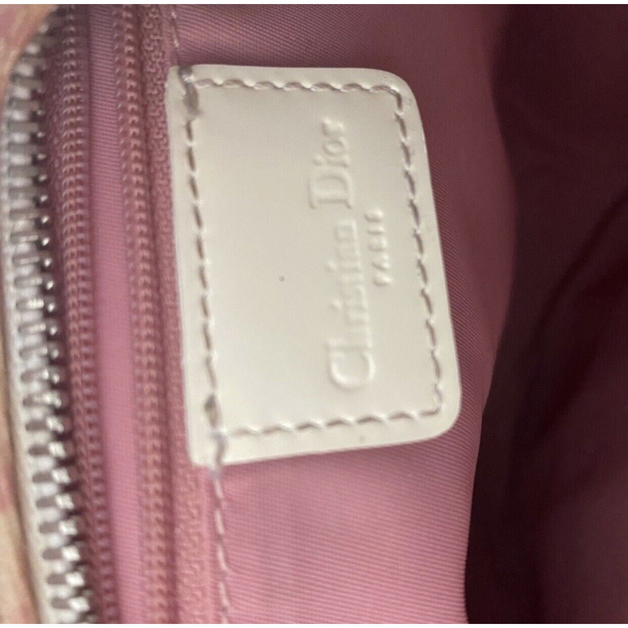 Close-up of a Dior label on a pink bag with a zipper.