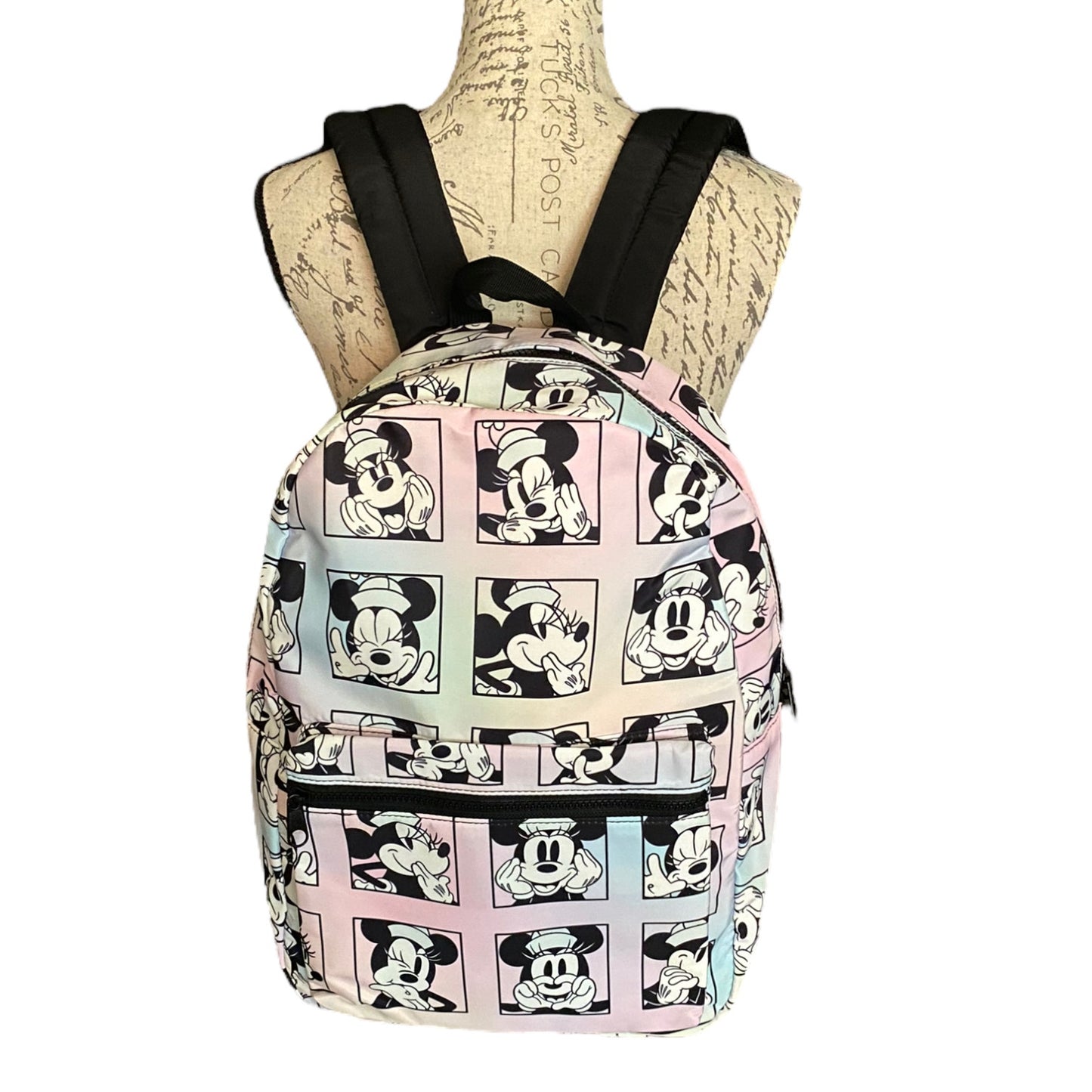 A backpack displayed on a vintage-style mannequin torso against a plain white background. The backpack features a repeating cartoon character print in pastel pink, blue, and yellow panels with black outlines and black shoulder straps.