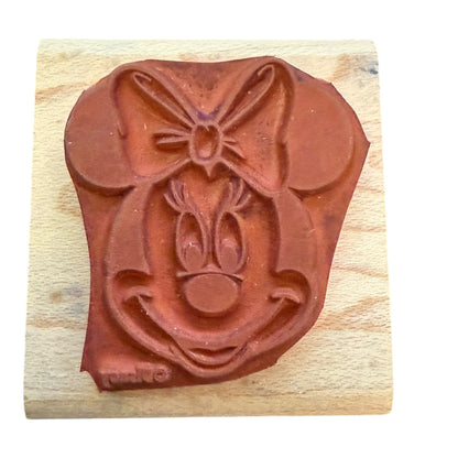 Red rubber stamp shaped like Minnie Mouse with a bow on a wooden block
