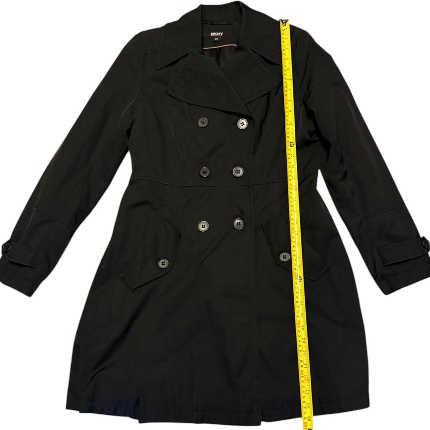 Black trench coat with a measuring tape draped over it on a white background