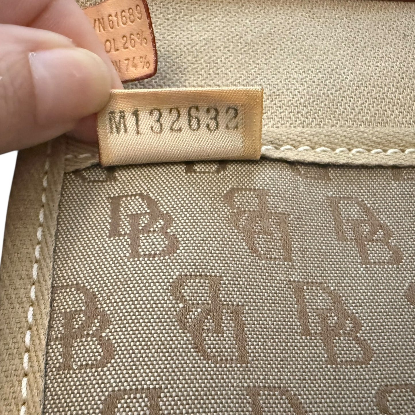 Close-up of a brown fabric with a brand logo and a hand holding a label with numbers.