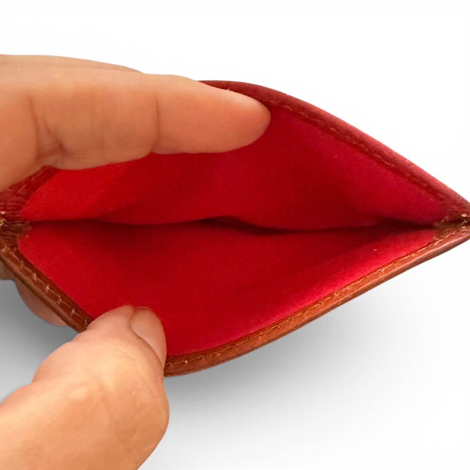 Hand holding an open leather wallet with a red interior on a white background
