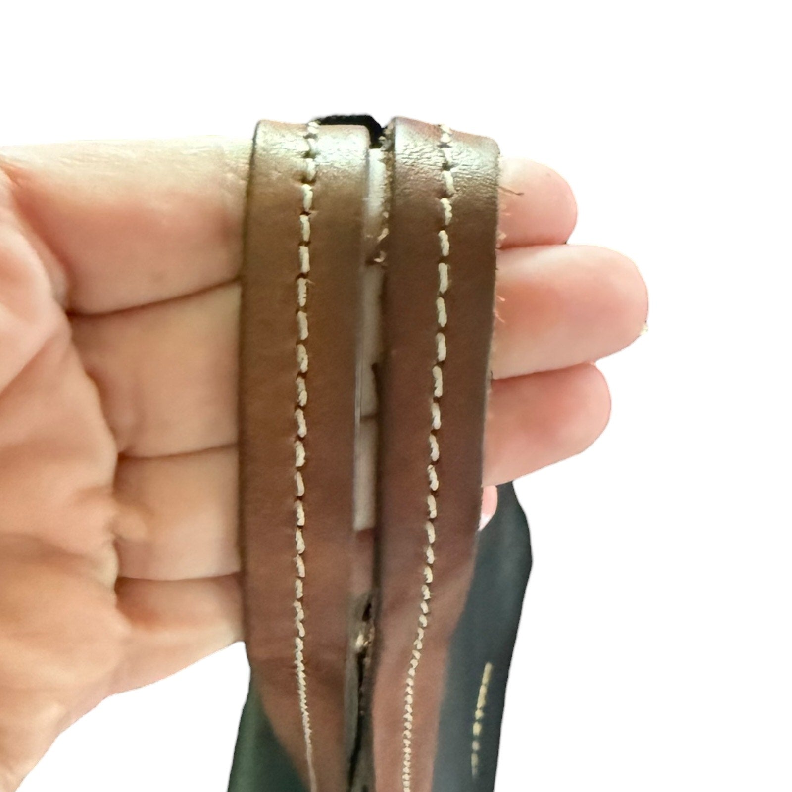 Close-up of a hand holding brown leather strap with stitching detail.