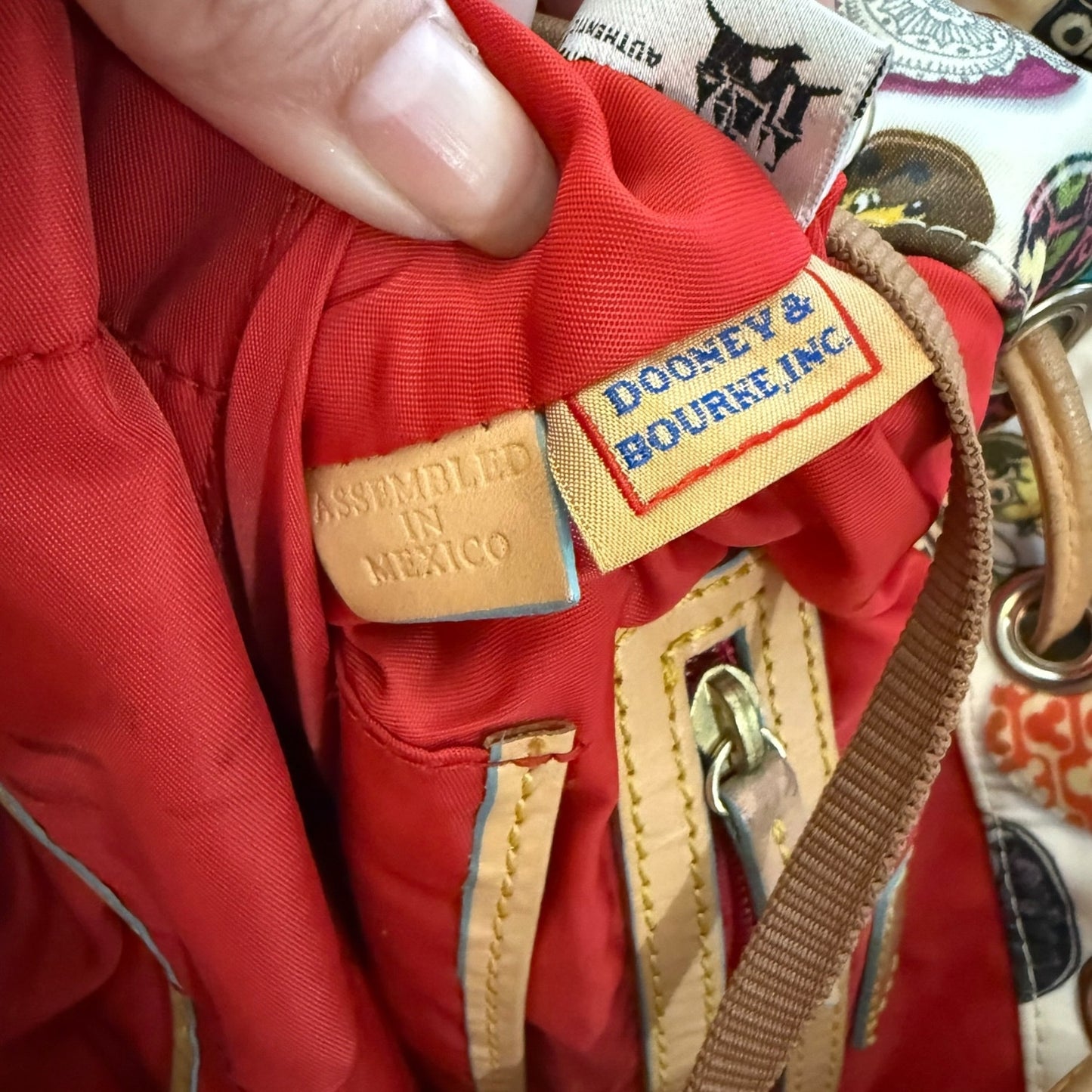 Close-up of a red interior of bag with 'Dooney & Bourke' label and 'Assembled in Mexico' tag.