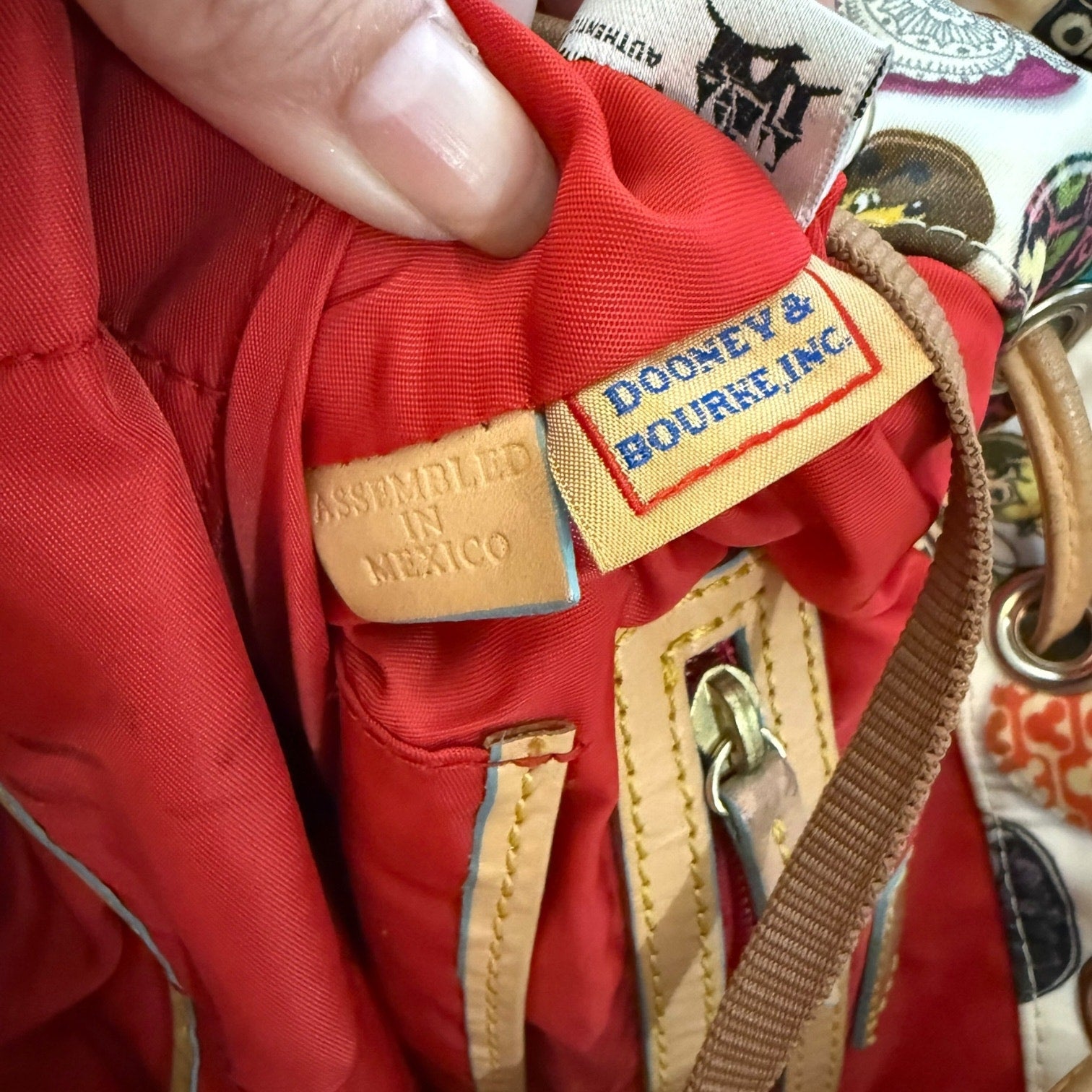 Close-up of a red interior of bag with 'Dooney & Bourke' label and 'Assembled in Mexico' tag.