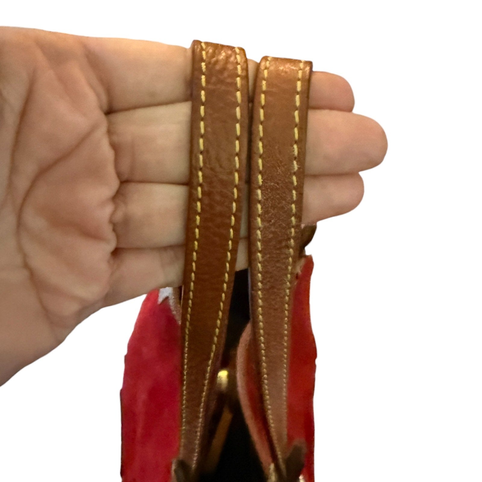 Close-up of a hand holding a red bag with brown leather strap against a white background