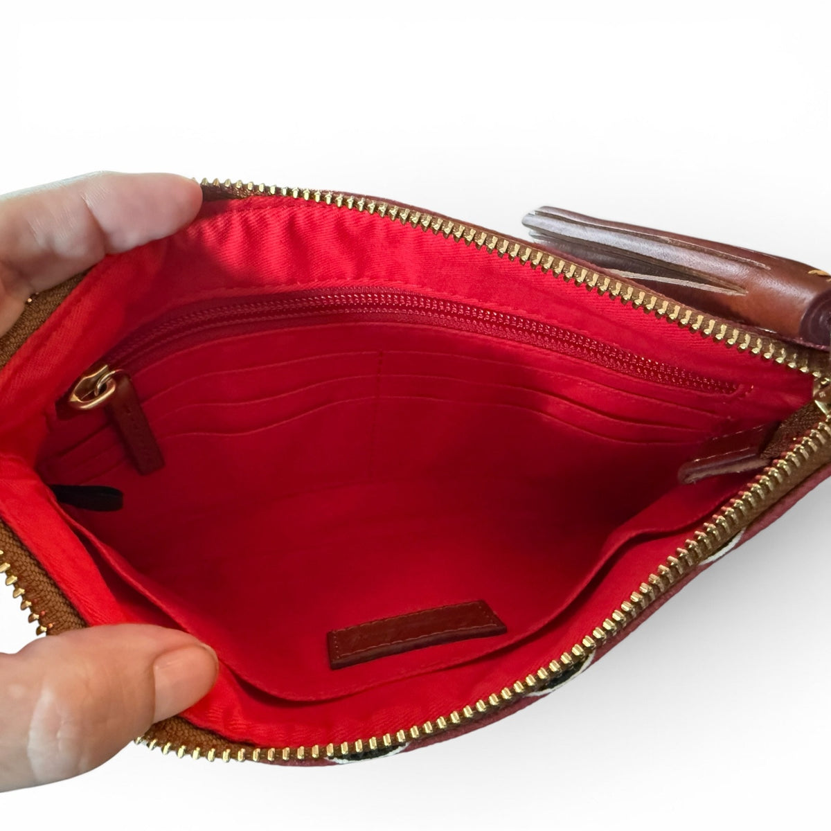 Red pouch interior showing pockets with gold zipper held open by a hand on a white background