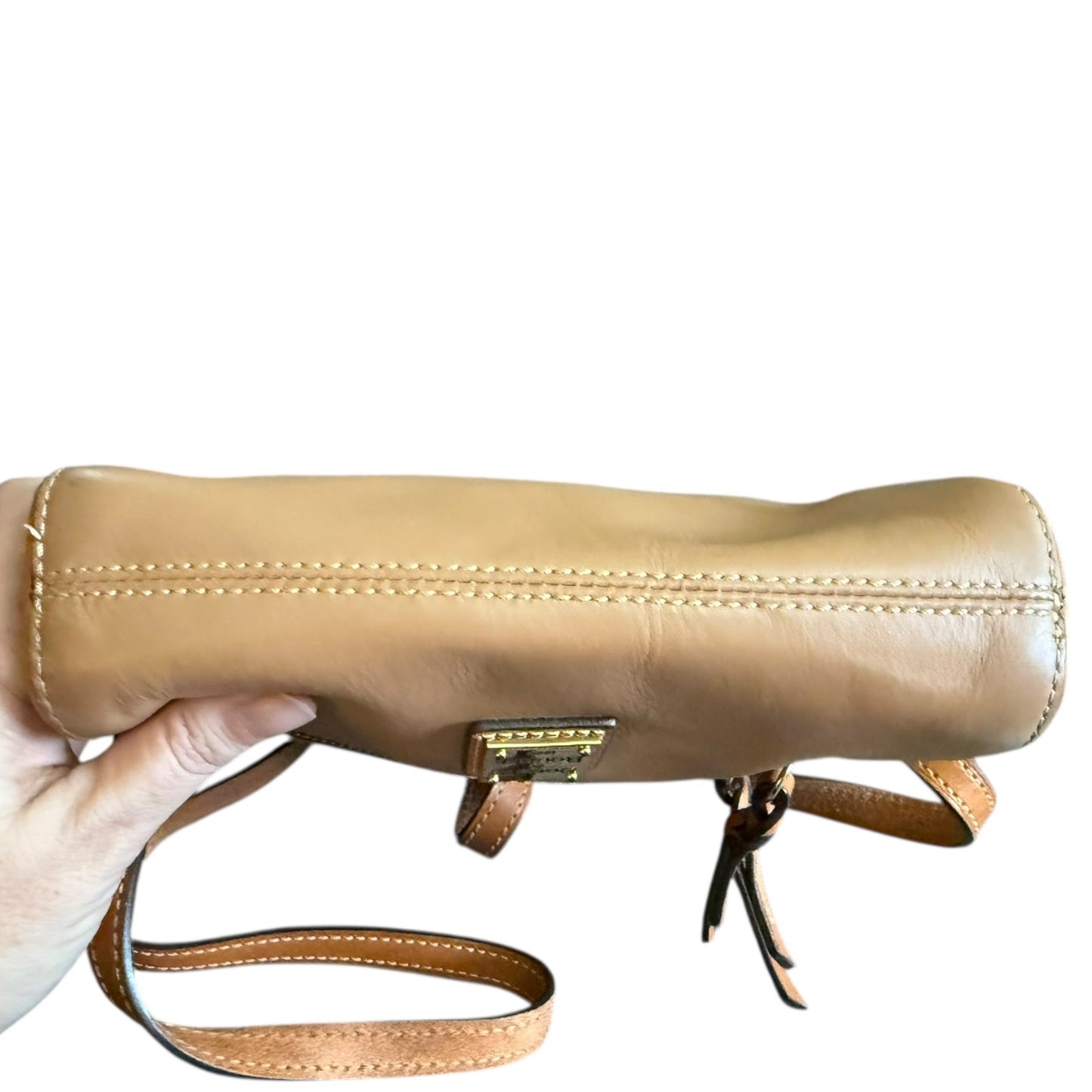 Bottom of brown leather handbag with a strap held by a hand on a white background