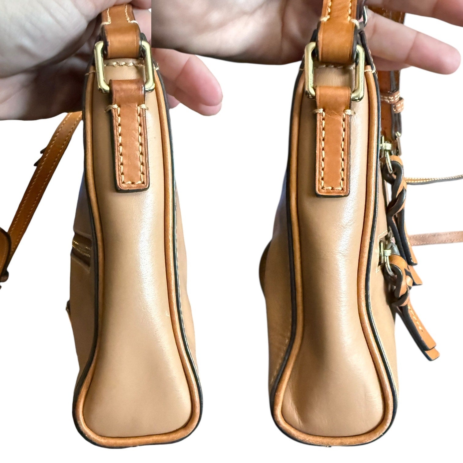Side view of brown leather handbag with gold hardware held by a person.