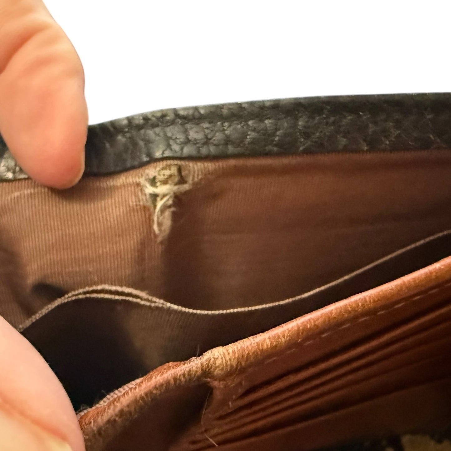 Close-up of a brown leather wallet with issues, held by a hand.