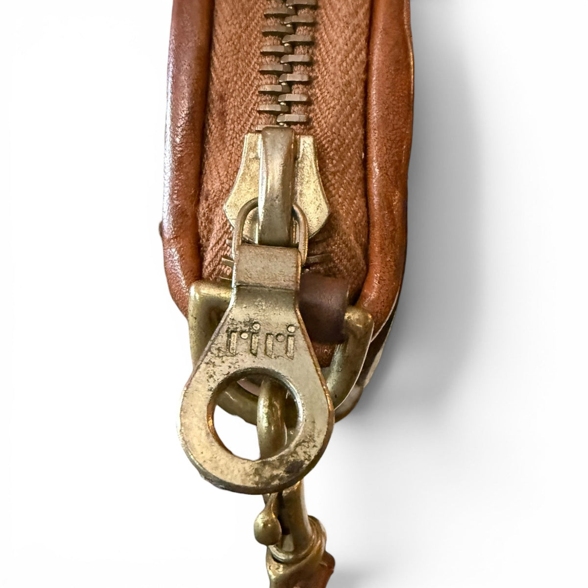 Close-up of a brown leather wallet with a brass zipper pull on a white background