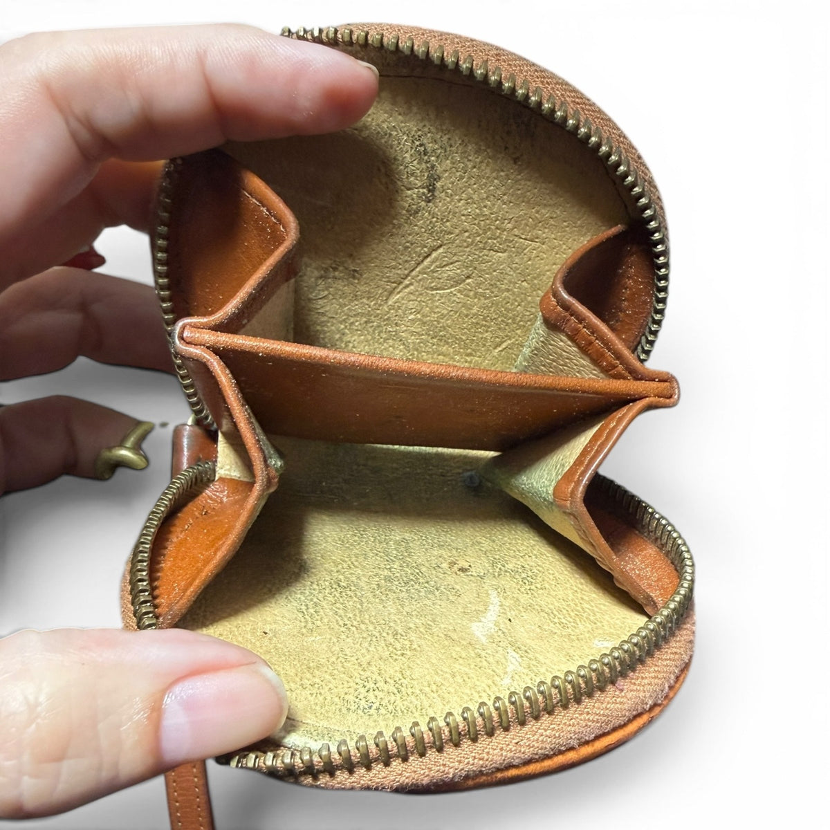 Open brown leather pouch wallet  with beige  interior, held by a hand on a white background