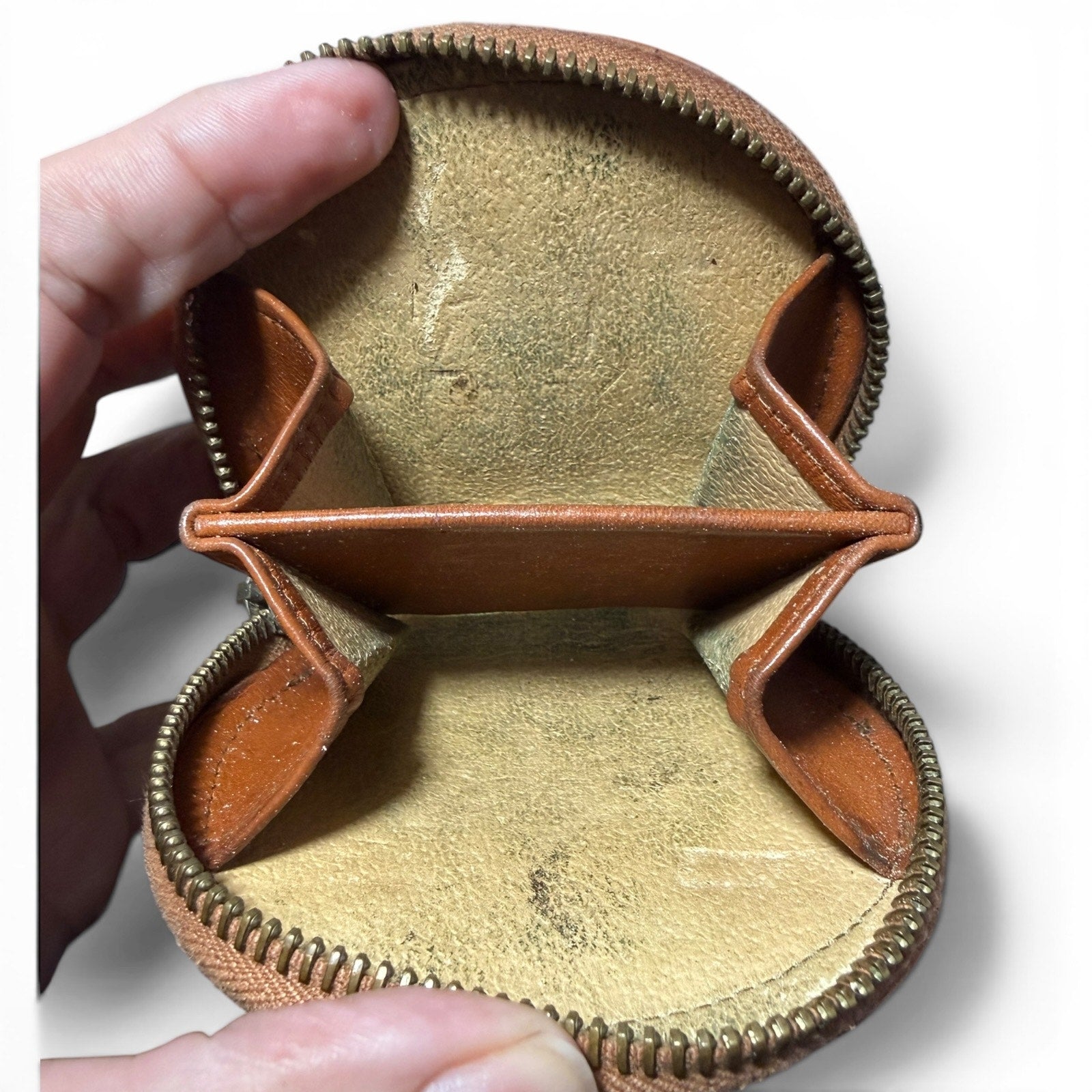 Close-up of a brown leather coin purse wallet with beige interior, held by a hand.