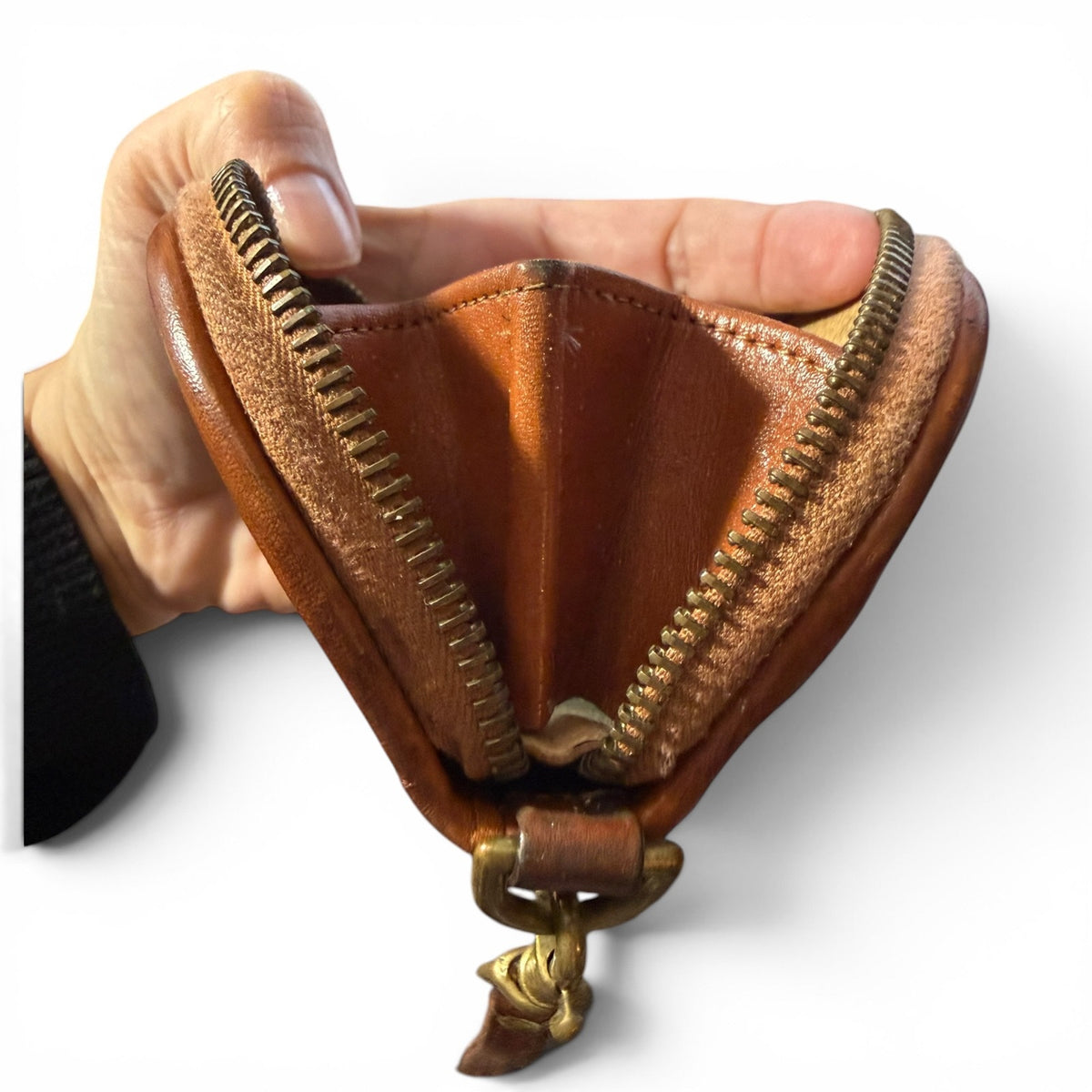 Brown leather wallet side view with gold zipper held by a hand on a white background
