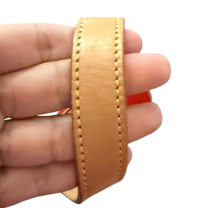 Tan leather strap held between fingers on a white background