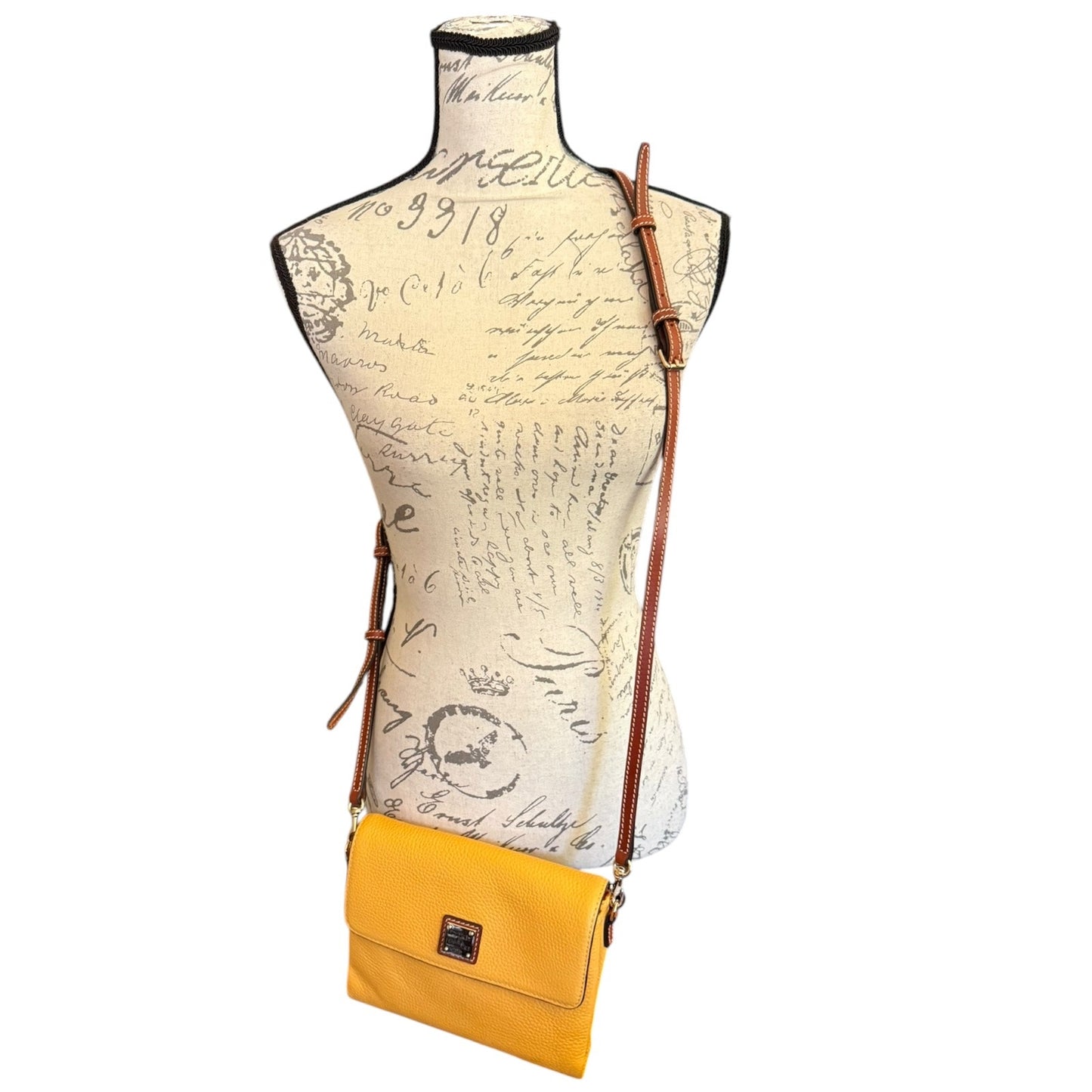 A yellow crossbody bag with a brown leather strap, displayed on a vintage-style printed dress form mannequin against a white background.