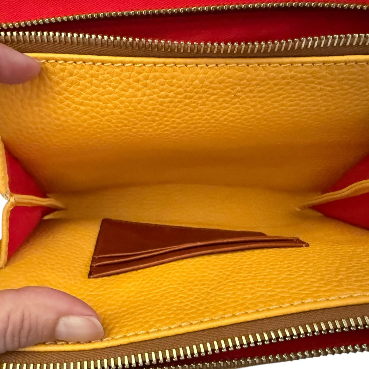 Close-up of the interior of a yellow pebbled leather purse , showing a brown leather card slot, gold-tone zipper, and red lining.