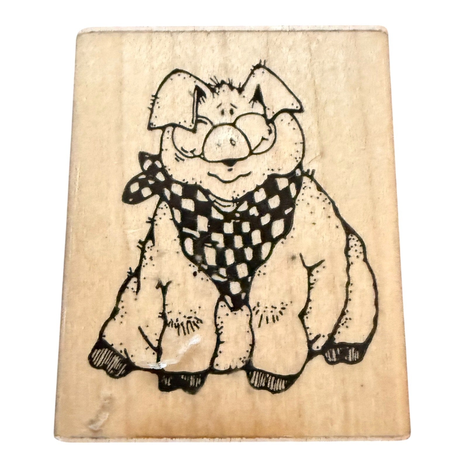 A wooden rubber stamp block featuring a cartoon pig wearing a black and white checkered bandana, shown on a plain white background.
