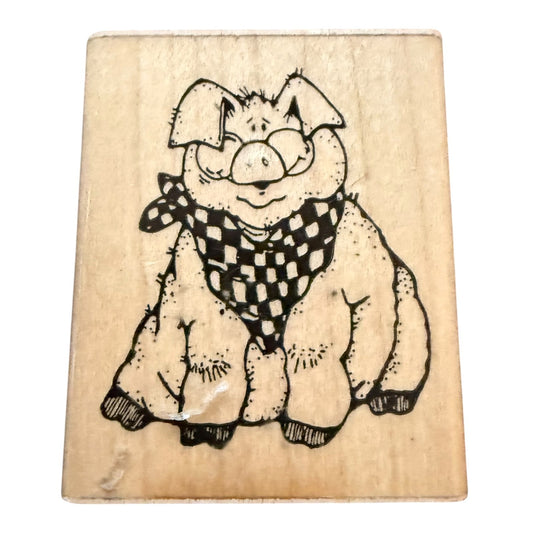 A wooden rubber stamp block featuring a cartoon pig wearing a black and white checkered bandana, shown on a plain white background.