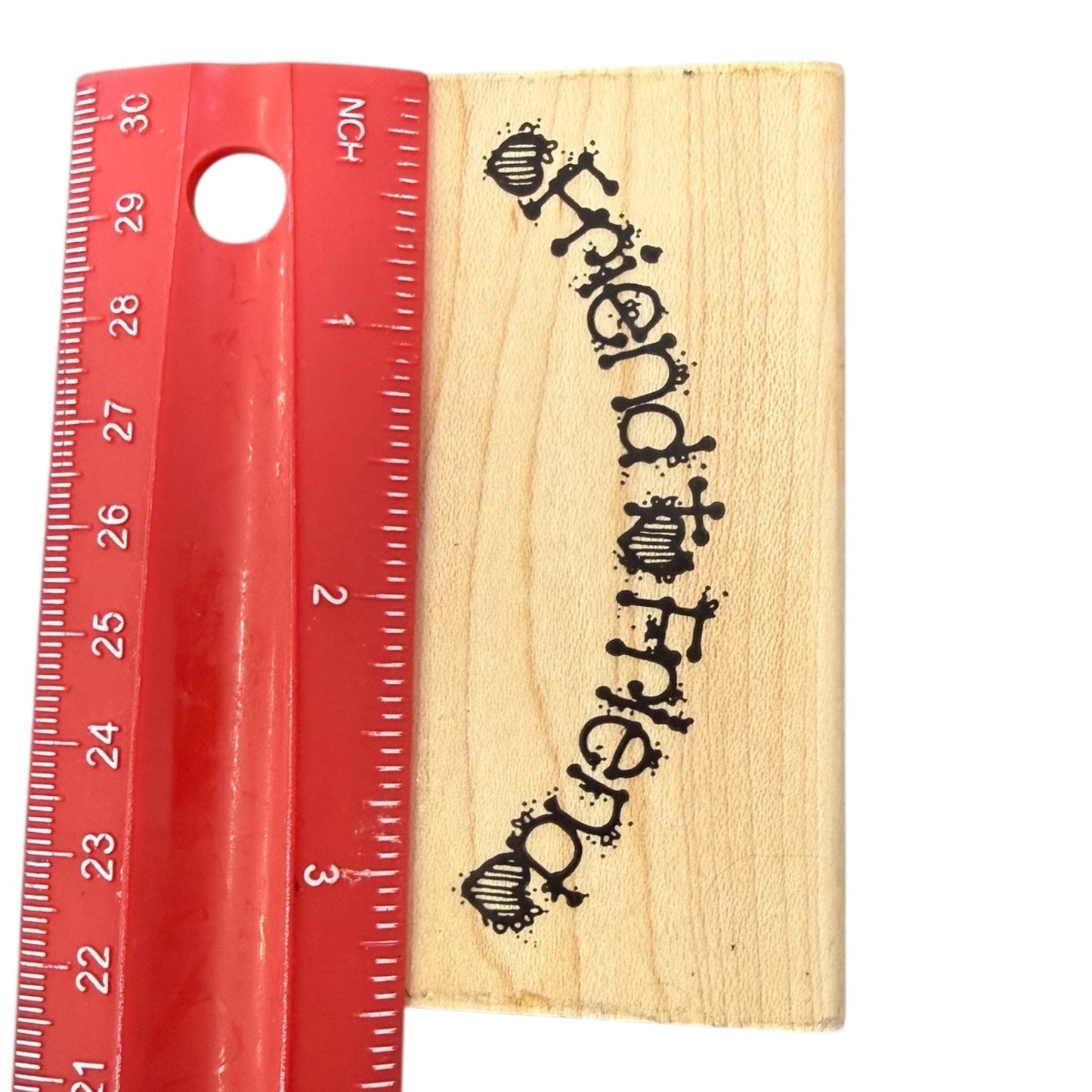 Wooden block with 'Friend to Friend' engraving next to a red ruler on a white background