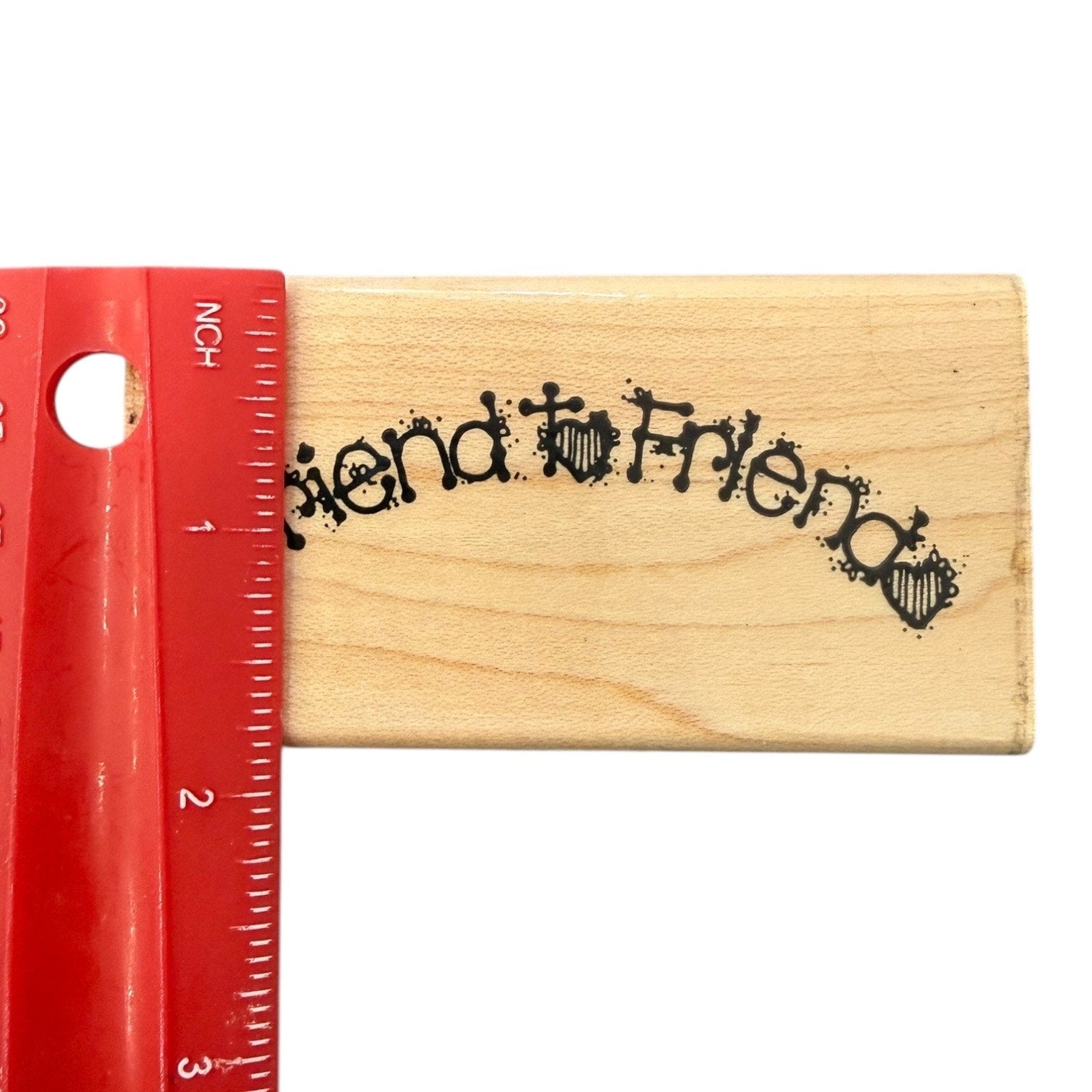 Wooden stamp with 'Friend to Friends' text next to a red ruler on a white background