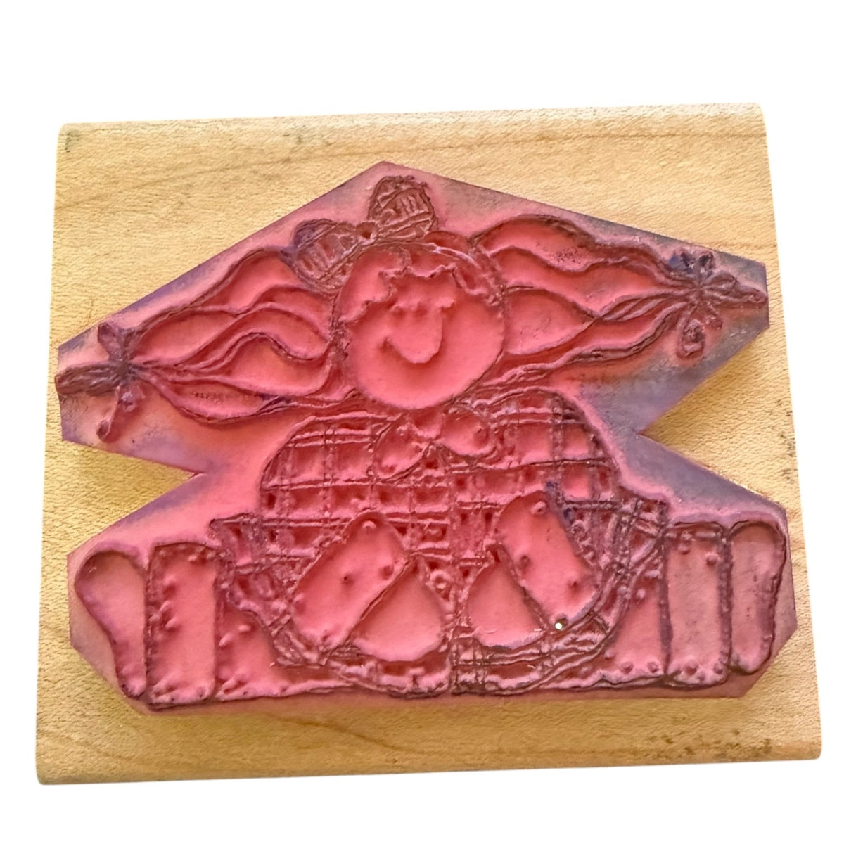 A pinkish-red rubber stamp with a whimsical character design, mounted on a light-colored wooden block against a white background.