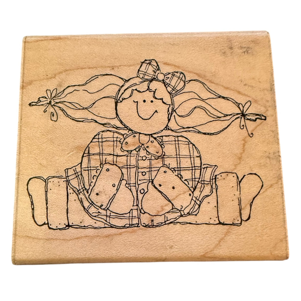 A square wooden rubber stamp block featuring a black line-art illustration of a smiling girl with long pigtails and a plaid dress, shown on a plain white background.