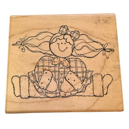 A square wooden rubber stamp block featuring a black line-art illustration of a smiling girl with long pigtails and a plaid dress, shown on a plain white background.