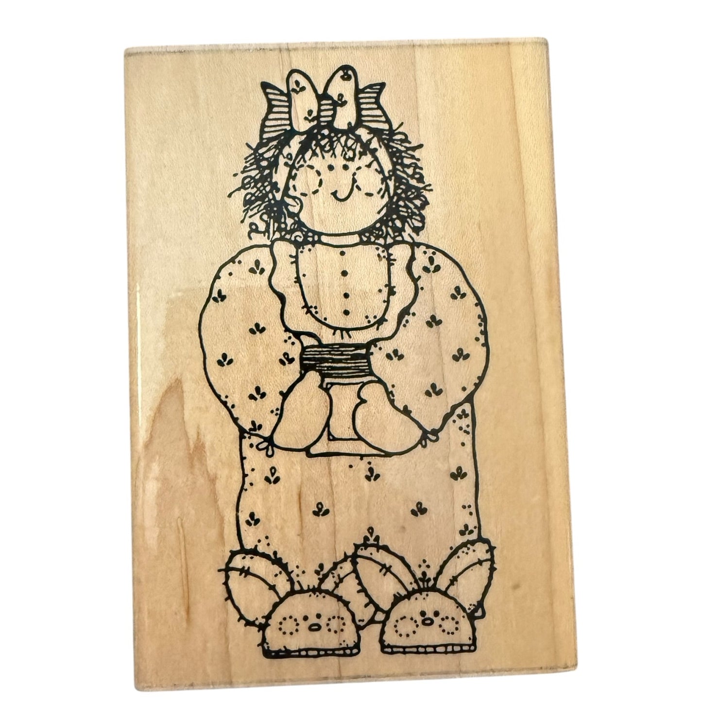 A rectangular wooden stamp block featuring a black line art illustration of a raggedy-faced doll girl in a patterned dress with bunny slippers, shown on a plain white background.