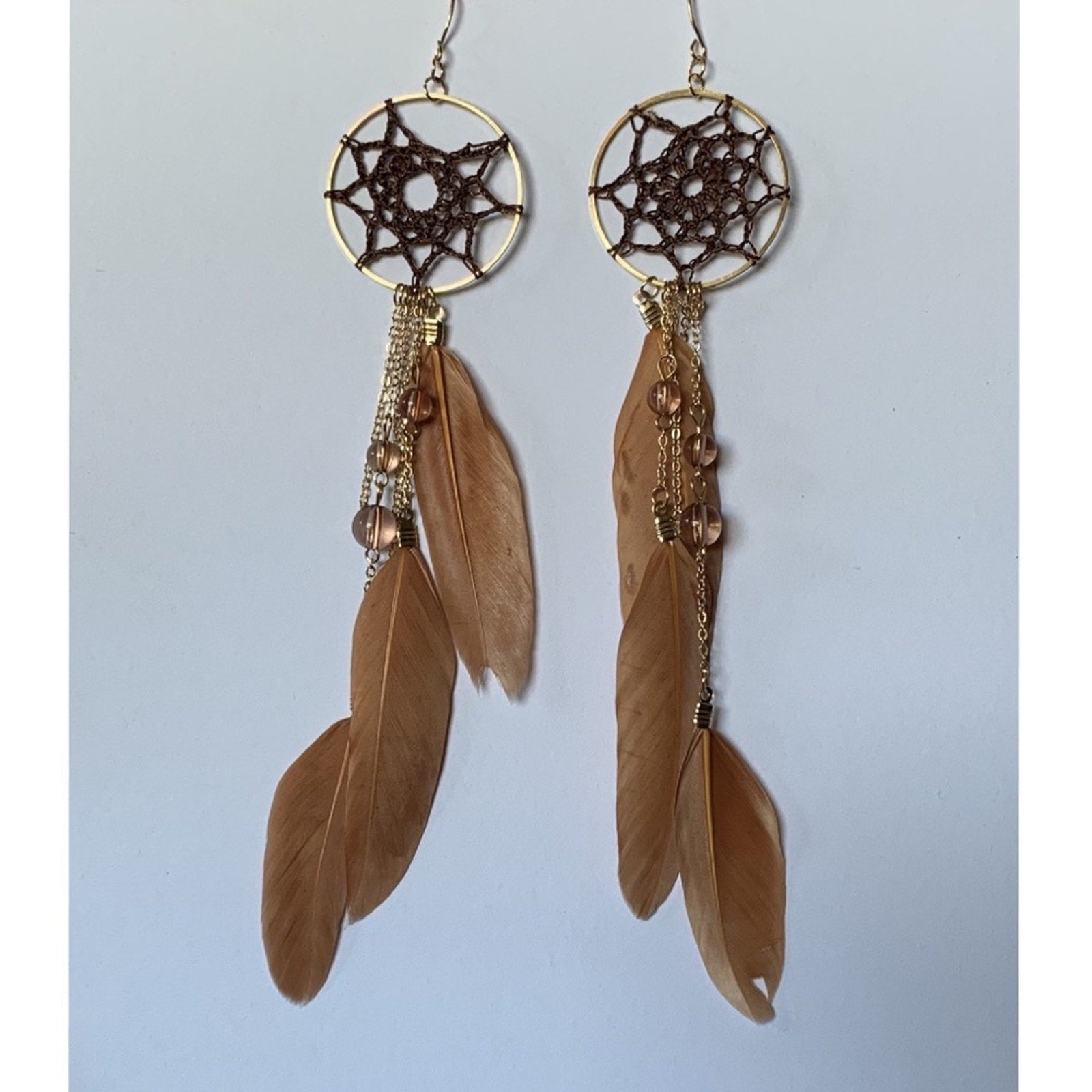 Pair of dreamcatcher earrings with feathers on a light gray background